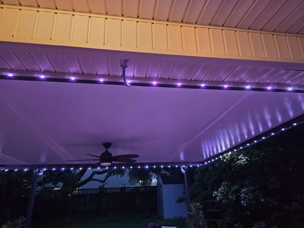 Soft purple lights illuminate a covered patio beneath a ceiling fan