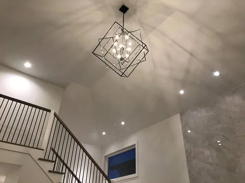 A modern staircase leads up to a stylish geometric chandelier casting intricate shadows