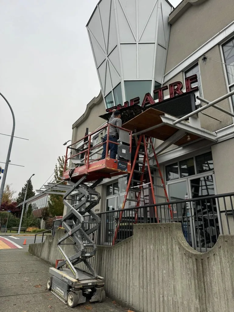 Commercial worker installing signage on a theater building using a lift