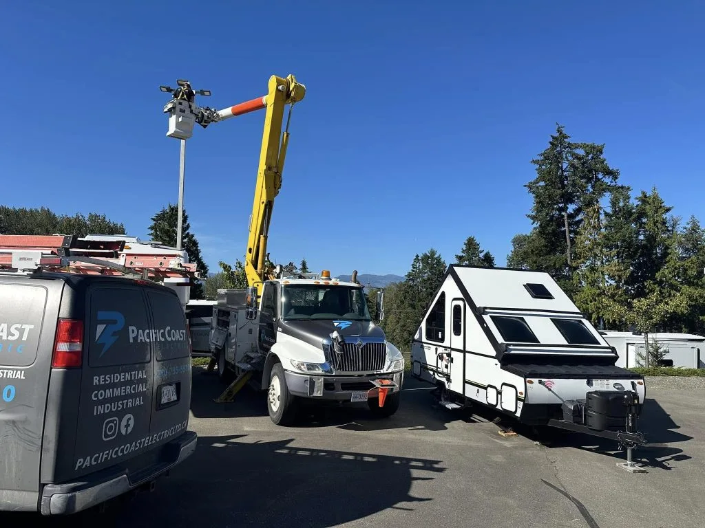 A utility truck with a raised crane is parked next to a camper trailer