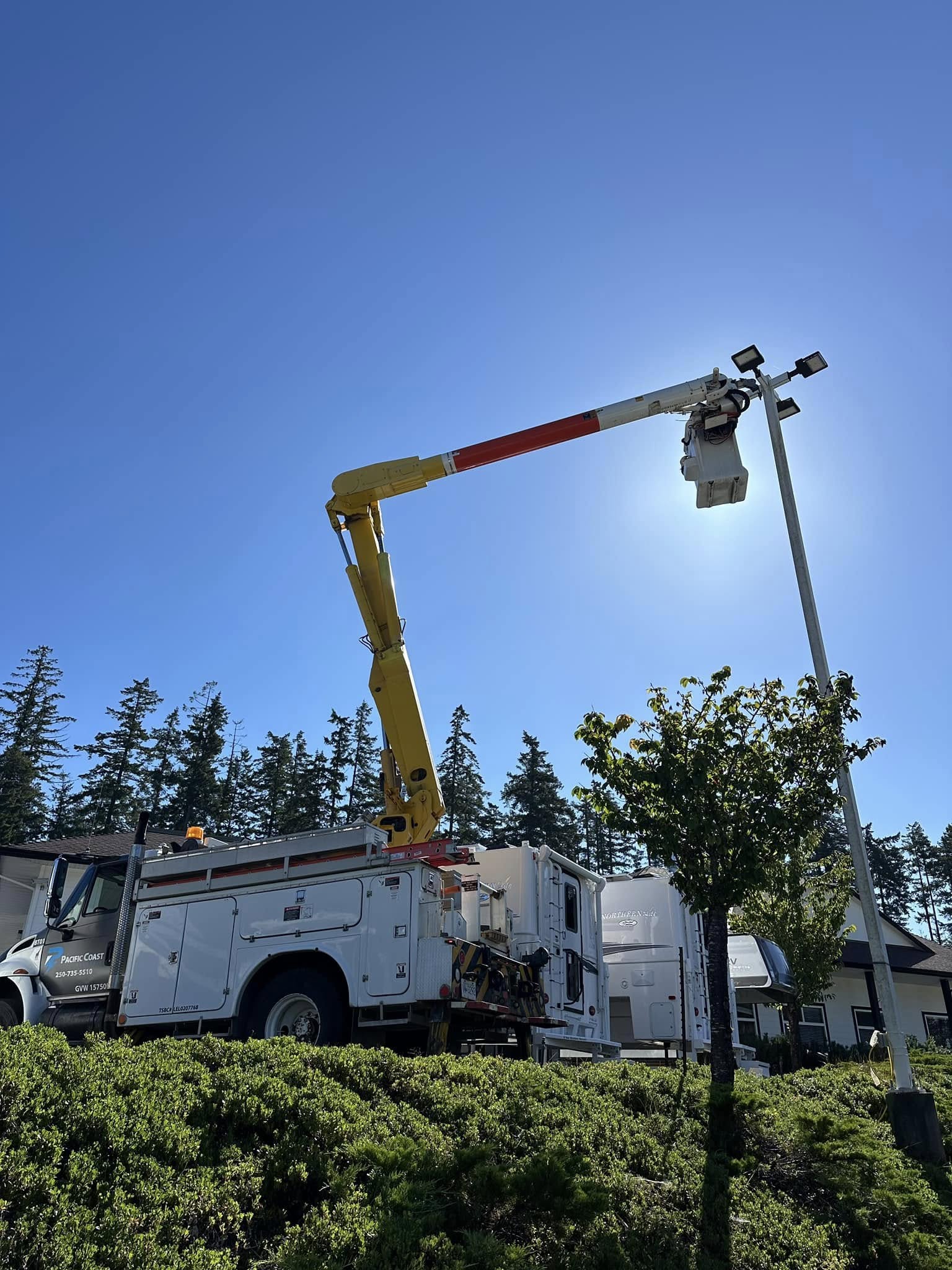 Electrical contractor using a cherry picker to reach a light pole against a clear blue sky