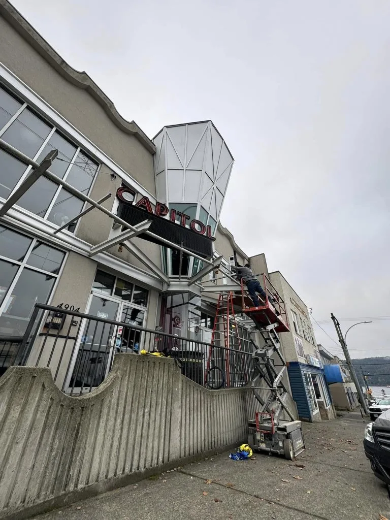 Electrical contractor repairing a sign on a scaffold outside a building