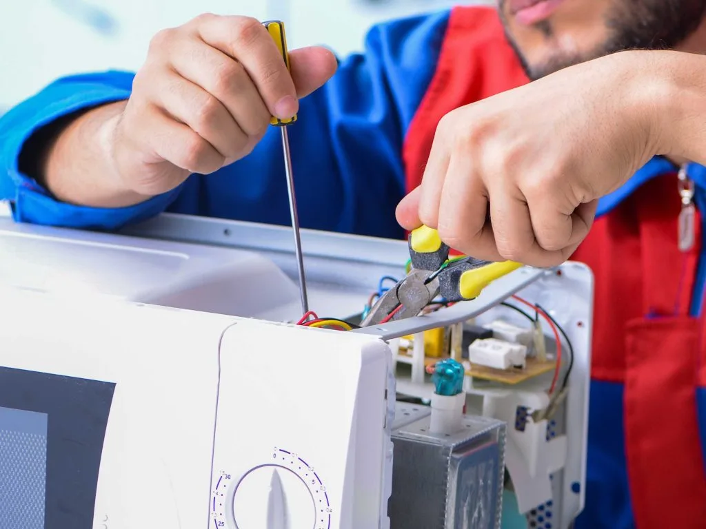 Electrical troubleshooting in action as a person repairs a microwave with tools