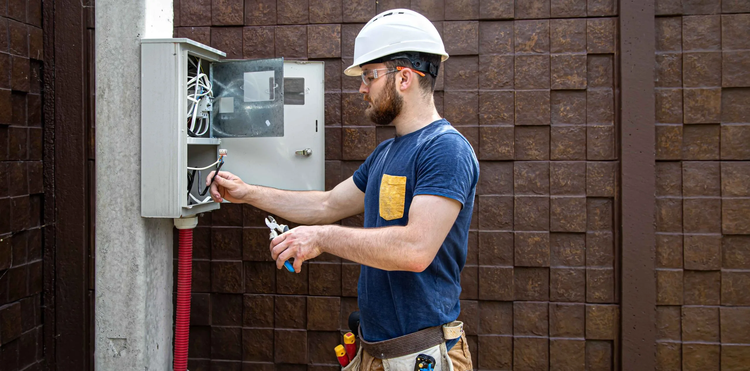 Electrical troubleshooting in progress as a man in a hard hat repairs equipment outside a building