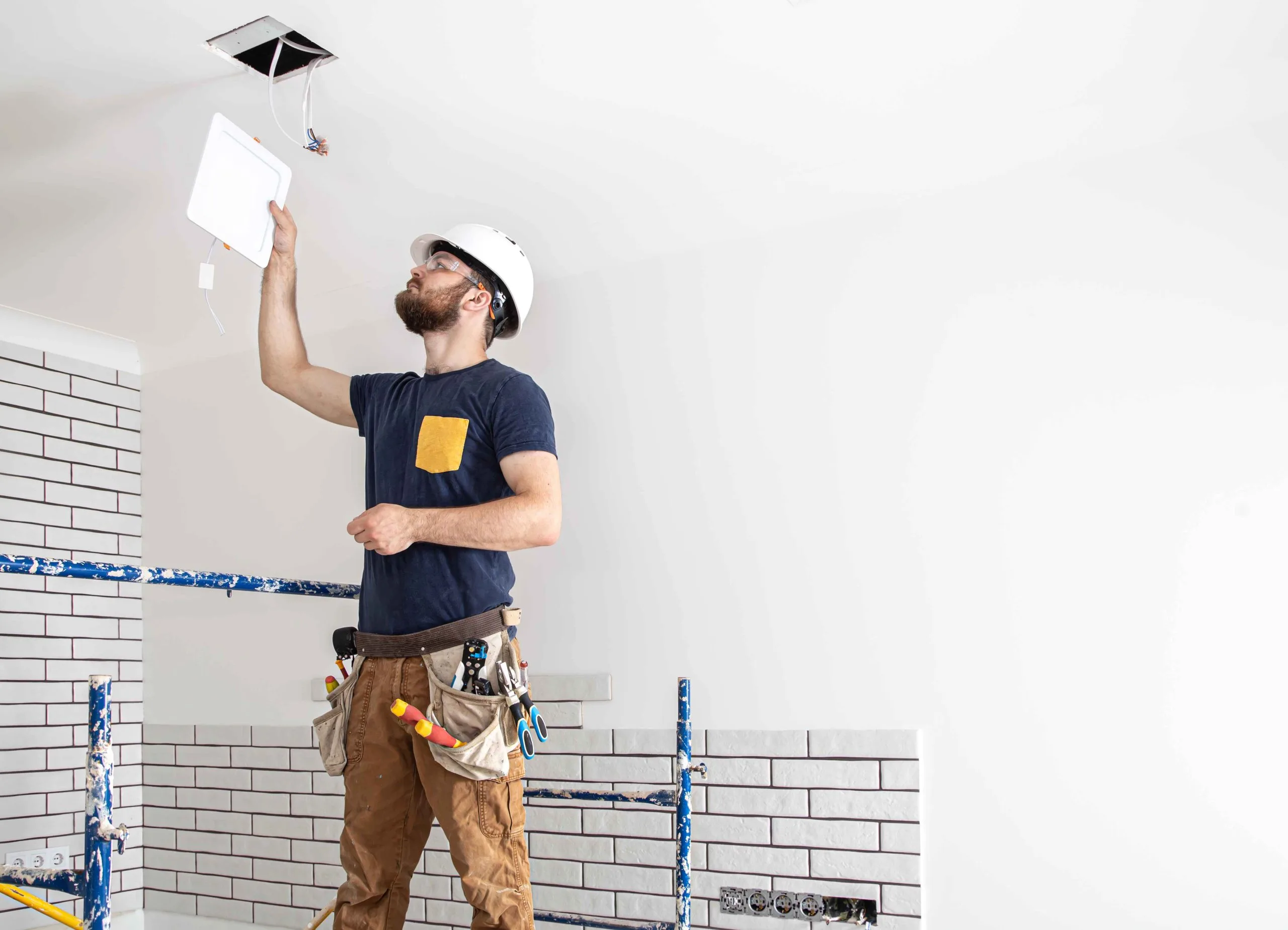 Construction worker inspecting ceiling for LED installs while reviewing project documents