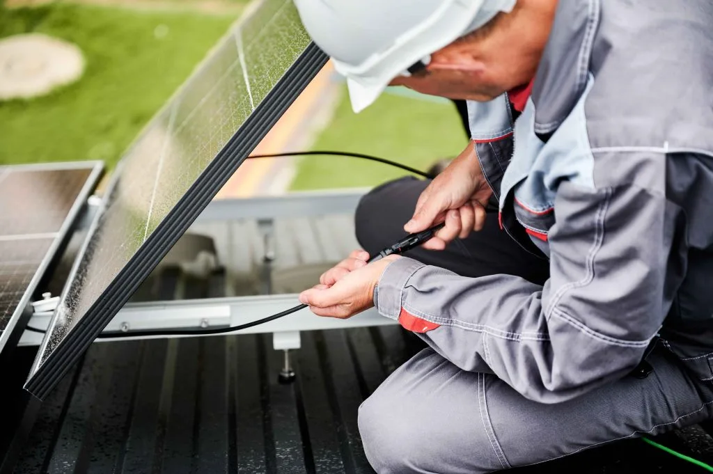 Technician performing solar panel installation on a rooftop, connecting cables carefully