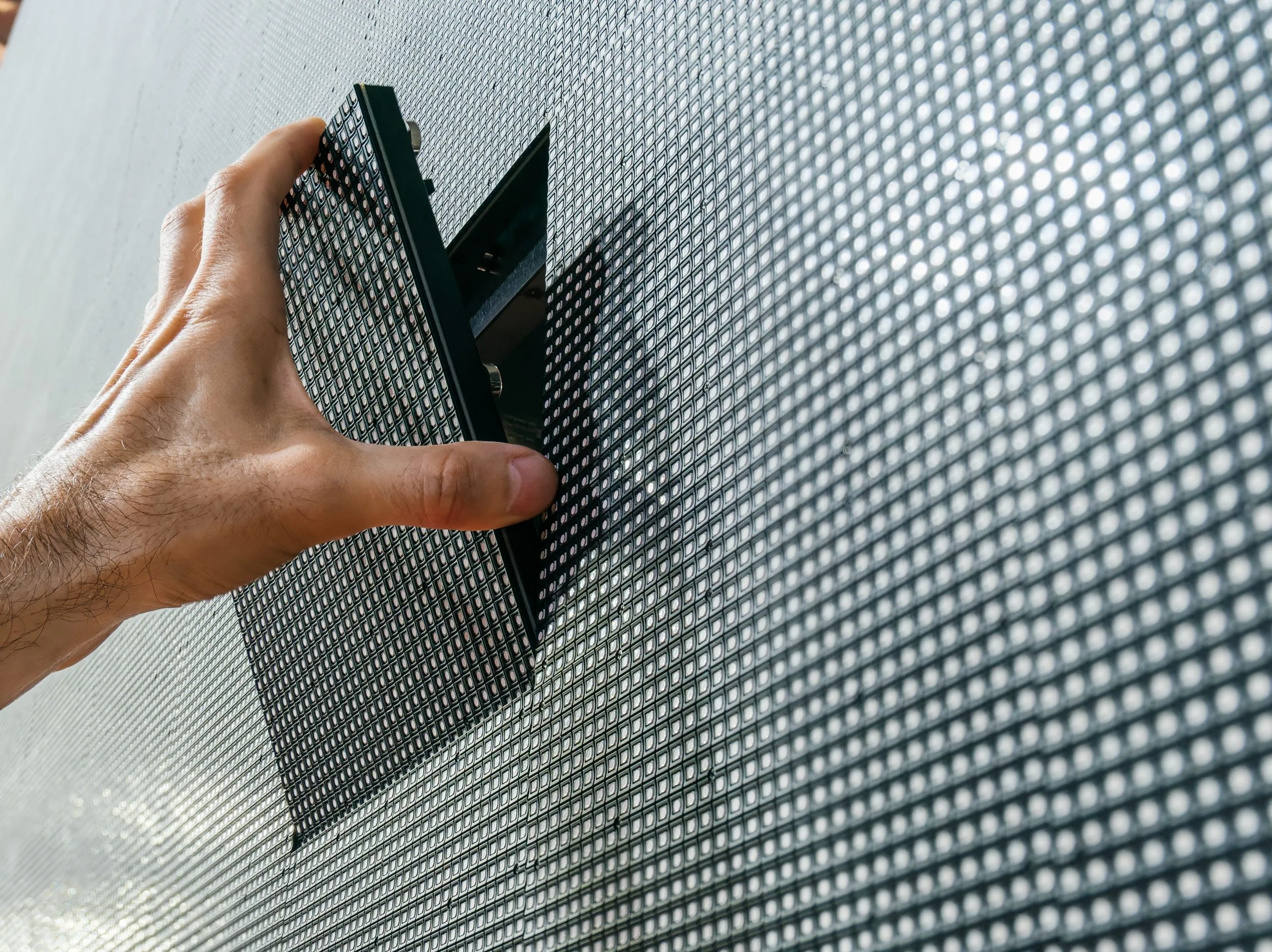 Hand placing a black panel during LED installs on a dotted surface