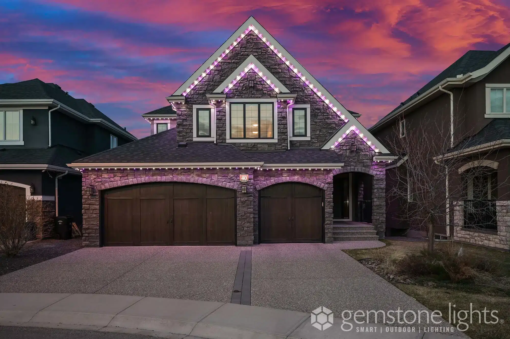 A beautifully lit house adorned with purple and white lights against a colorful sunset sky