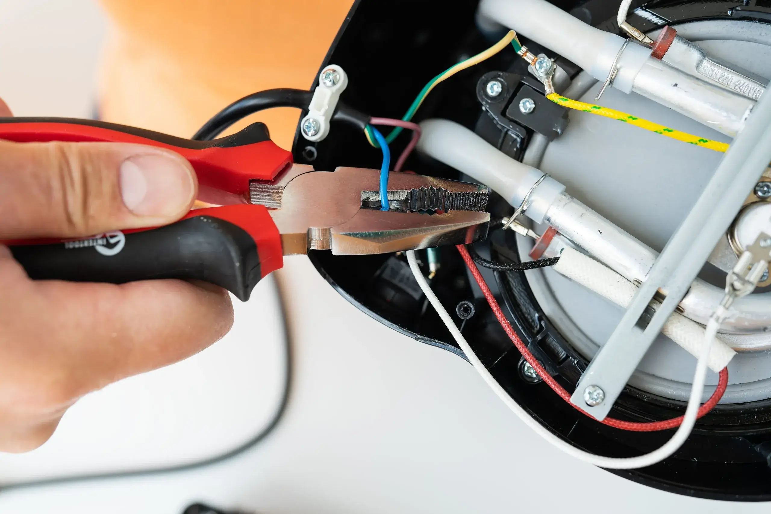 A person uses pliers to manipulate and connect colorful electrical wires