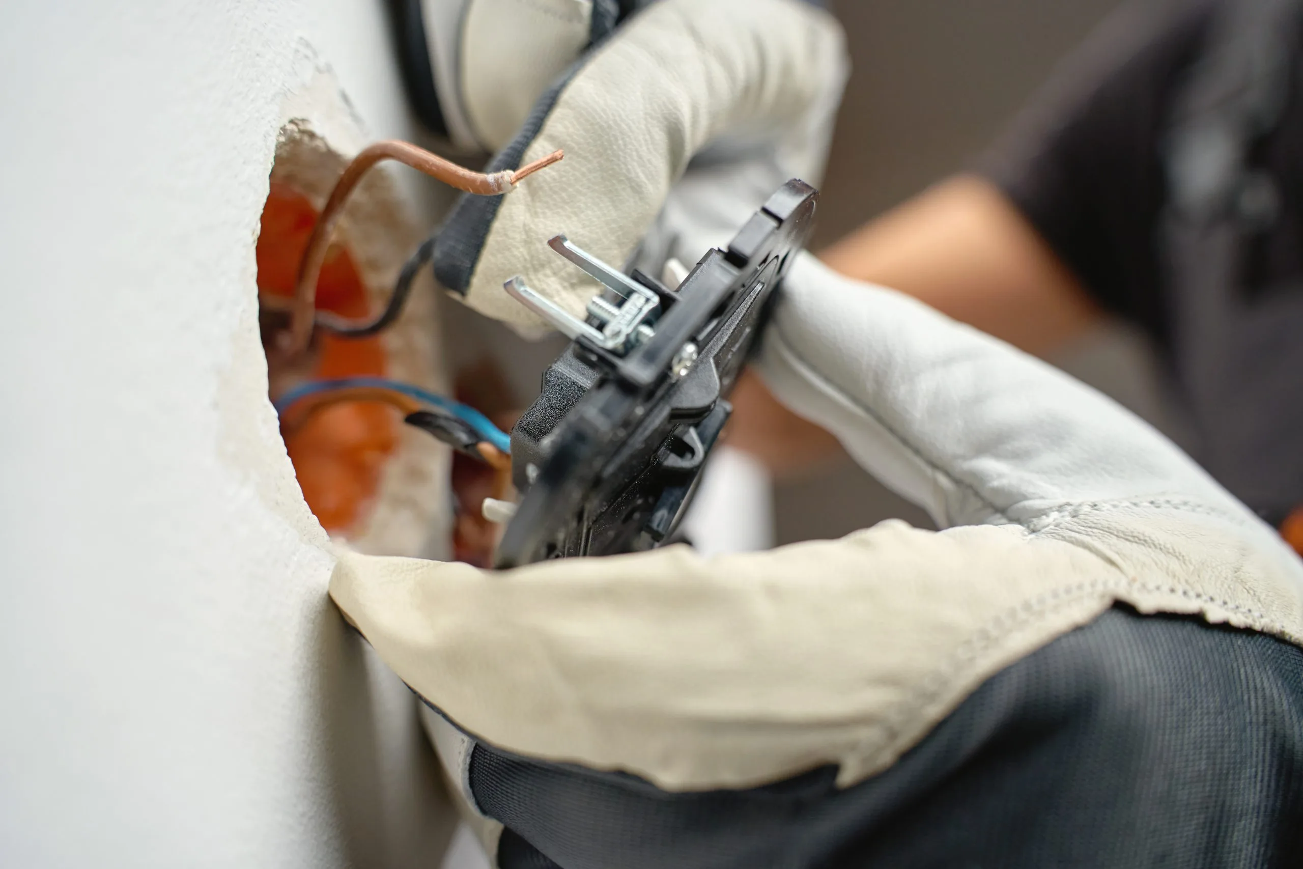 A person wearing gloves is installing an electrical switch into a wall